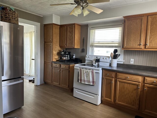 kitchen with freestanding refrigerator, white electric range oven, dark countertops, ceiling fan, and brown cabinetry