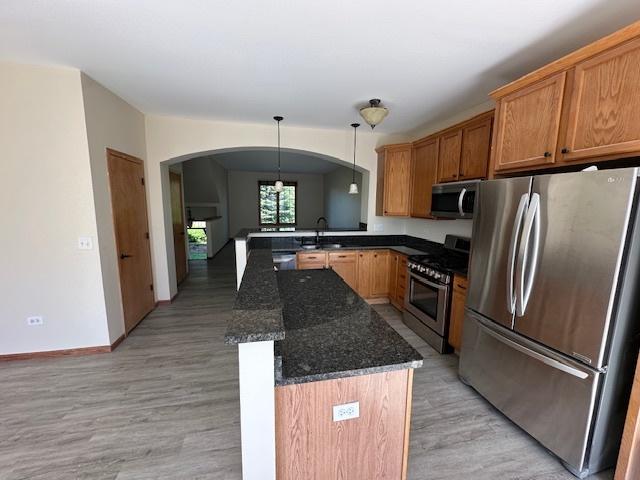 15810 Scotsglen Rd, Orland Park, IL 60462 - kitchen featuring appliances with stainless steel finishes, a sink, light wood-style flooring, arched walkways, and dark stone countertops
