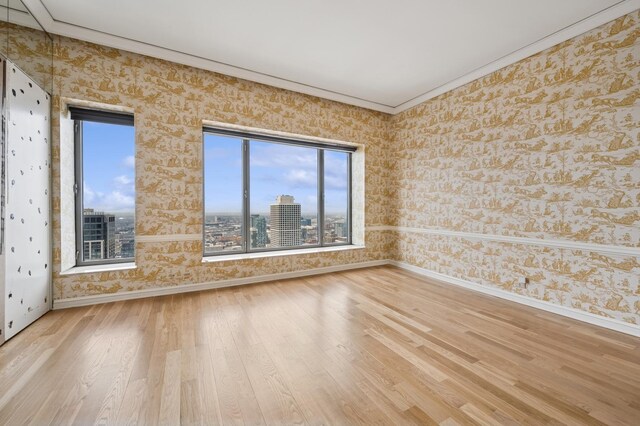 empty room with wallpapered walls, baseboards, wood finished floors, ornamental molding, and healthy amount of natural light