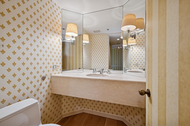 bathroom featuring wallpapered walls, wood finished floors, a sink, and toilet