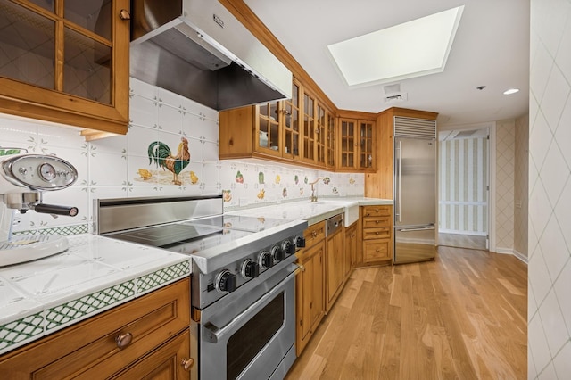 kitchen featuring premium appliances, brown cabinetry, under cabinet range hood, and light wood-style flooring