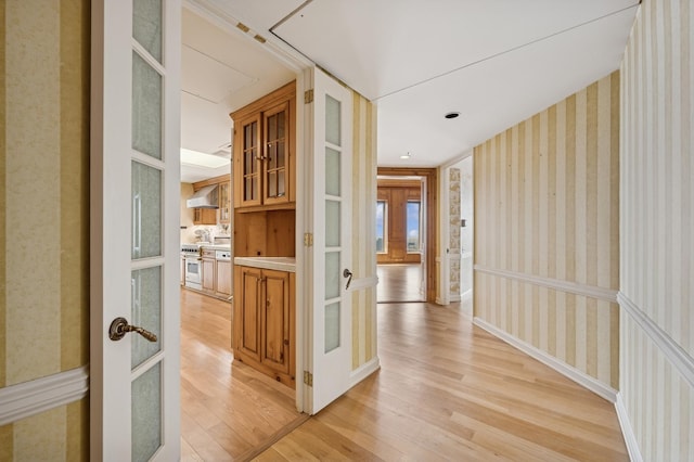 corridor with wallpapered walls, light wood finished floors, and french doors