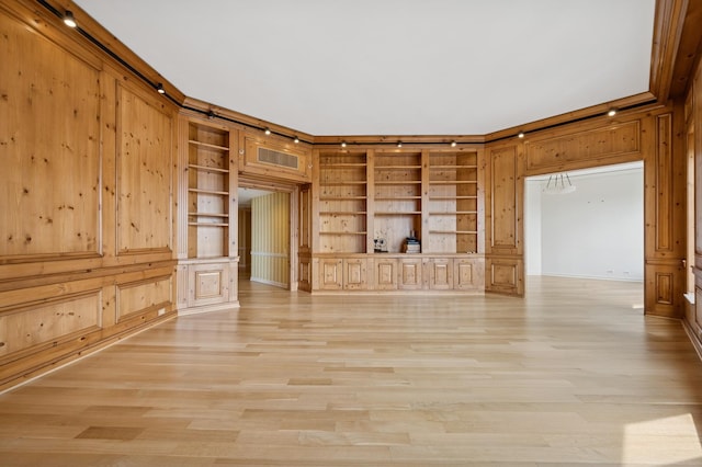 unfurnished living room with built in features, light wood-style flooring, ornamental molding, and wooden walls