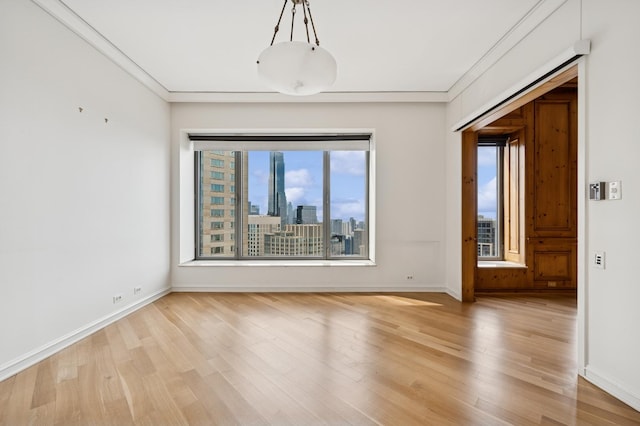 empty room with ornamental molding, light wood-style floors, and baseboards