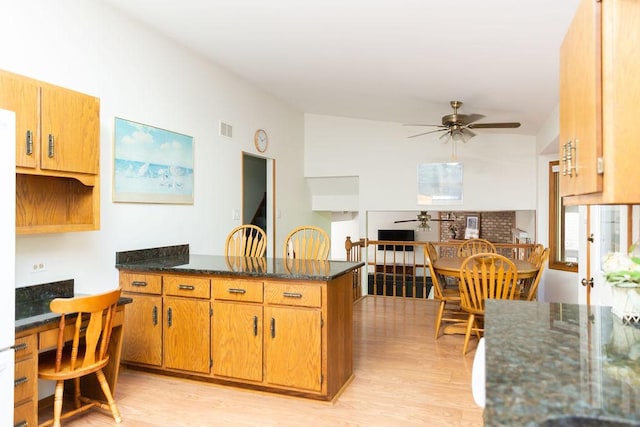 kitchen featuring a ceiling fan, a peninsula, light wood-type flooring, dark stone counters, and brown cabinetry