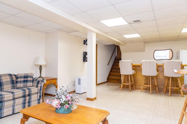 living room featuring a paneled ceiling, a dry bar, stairs, tile patterned floors, and baseboards