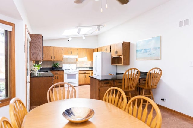 kitchen featuring white appliances, under cabinet range hood, vaulted ceiling, dark countertops, and backsplash