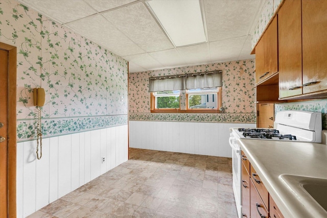 235 N Main St, Roberts, IL 60962 - kitchen featuring white range with gas stovetop, wallpapered walls, a drop ceiling, wainscoting, and a sink