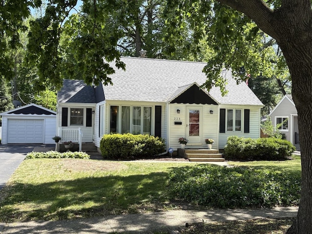 cape cod-style house with an outdoor structure, driveway, roof with shingles, a detached garage, and a front yard
