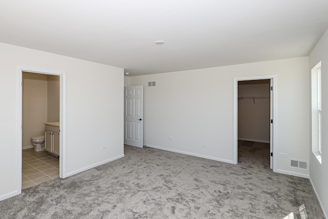 unfurnished bedroom featuring a spacious closet, light colored carpet, baseboards, a closet, and ensuite bathroom
