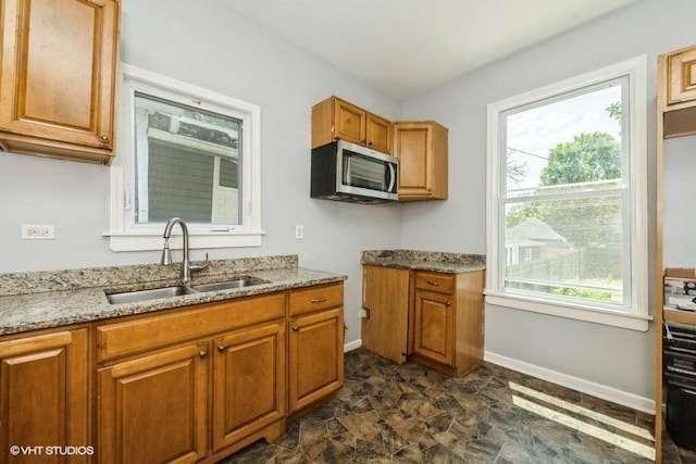 1505 E 76th Pl, Chicago, IL 60619 - kitchen with stainless steel microwave, light stone countertops, brown cabinetry, and healthy amount of natural light