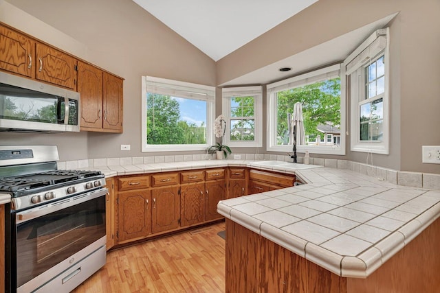 3513 Harris Dr, Joliet, IL 60431 - kitchen featuring stainless steel appliances, a sink, light wood finished floors, vaulted ceiling, and brown cabinets