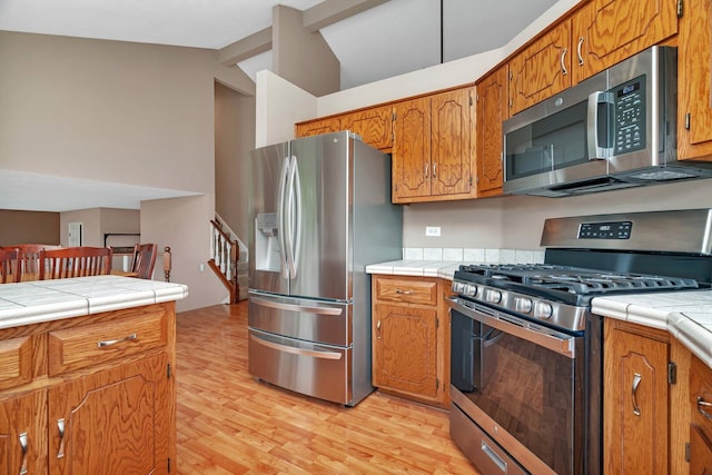 3513 Harris Dr, Joliet, IL 60431 - kitchen featuring stainless steel appliances, lofted ceiling, light wood-style flooring, brown cabinets, and tile countertops
