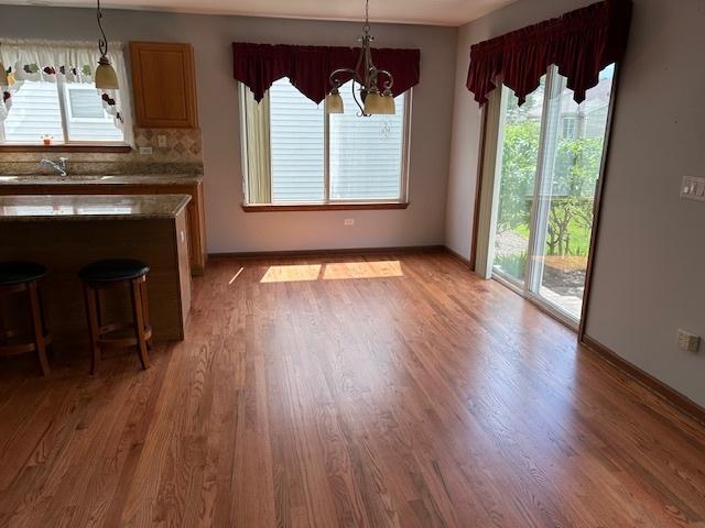 13804 Ironwood Dr, Plainfield, IL 60544 - kitchen featuring light wood-type flooring, hanging light fixtures, baseboards, and a breakfast bar area