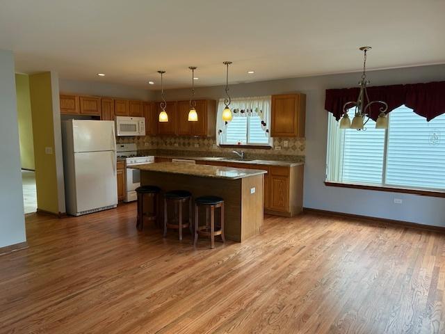 13804 Ironwood Dr, Plainfield, IL 60544 - kitchen featuring white appliances, a chandelier, backsplash, a kitchen island, and light wood finished floors