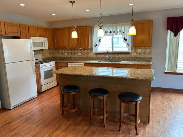 13804 Ironwood Dr, Plainfield, IL 60544 - kitchen with white appliances, a sink, a breakfast bar, decorative backsplash, and light wood finished floors