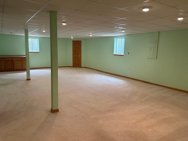 13804 Ironwood Dr, Plainfield, IL 60544 - basement with light colored carpet, plenty of natural light, electric panel, baseboards, and a drop ceiling