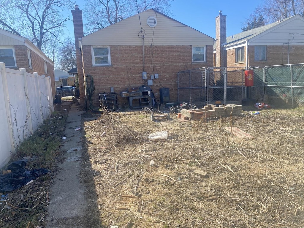 back of house featuring brick siding, fence, and a chimney