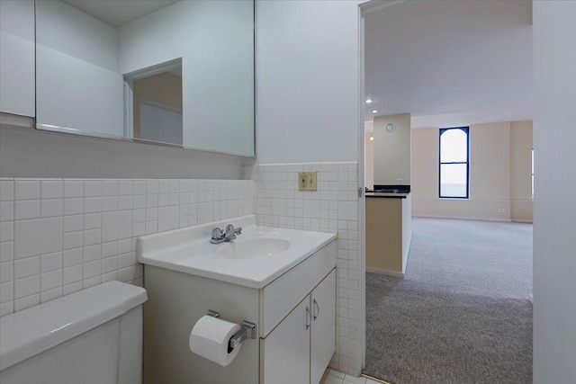 bathroom with tile walls, toilet, vanity, and a wainscoted wall