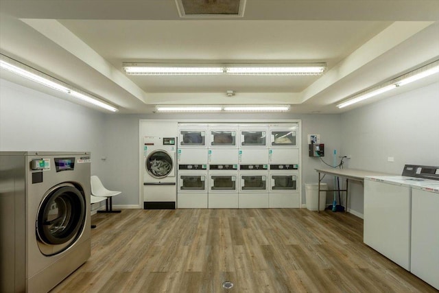 community laundry room with stacked washer / dryer, independent washer and dryer, light wood-style floors, and baseboards