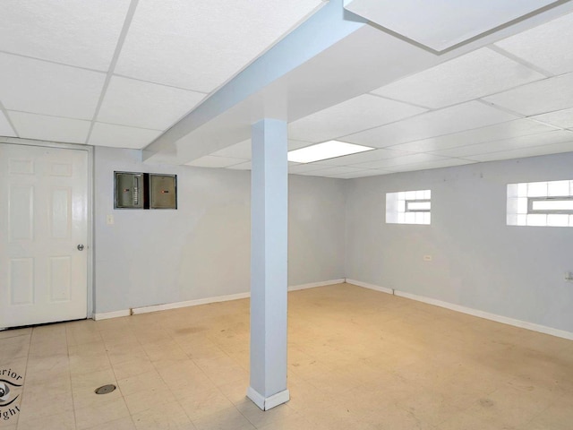 basement with a paneled ceiling, baseboards, and tile patterned floors