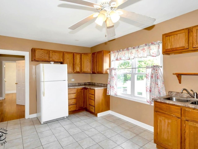 kitchen featuring freestanding refrigerator, brown cabinetry, ceiling fan, and baseboards