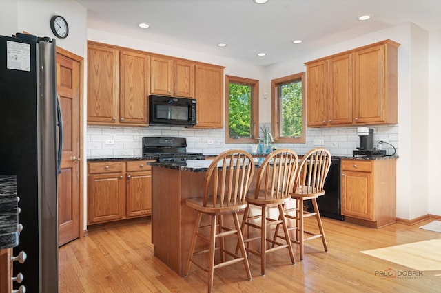 1701 Driftwood Ln, Crystal Lake, IL 60014 - kitchen with black appliances, light wood-style flooring, a kitchen island, decorative backsplash, and a kitchen breakfast bar