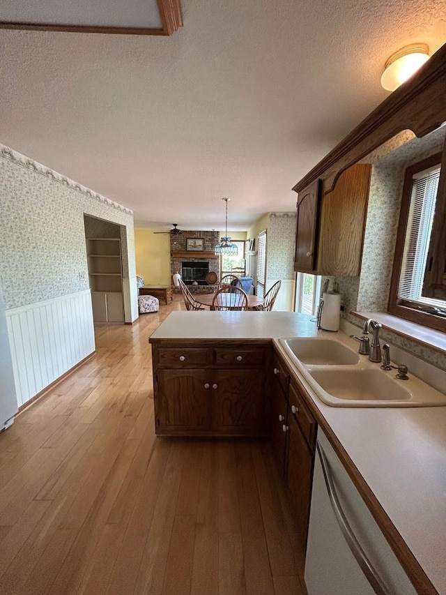 122 San Carlos Rd, Minooka, IL 60447 - kitchen featuring wallpapered walls, a sink, dishwasher, wainscoting, and a stone fireplace