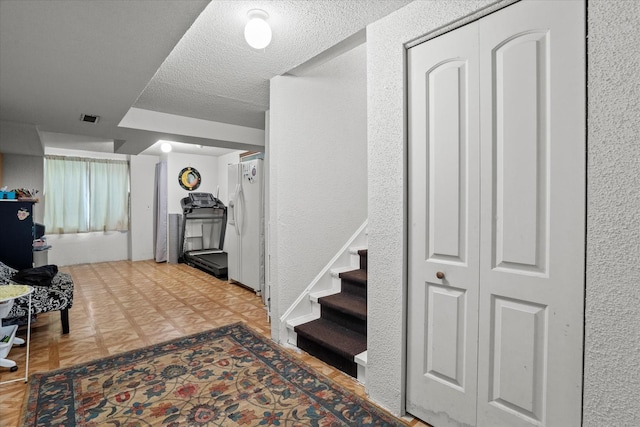 hall featuring a textured wall, a textured ceiling, and stairway
