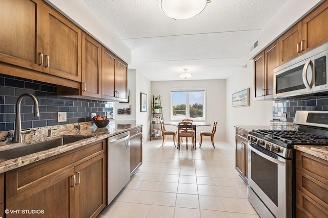 6807 N Milwaukee Ave Unit 204, Niles, IL 60714 - kitchen with stainless steel appliances, a sink, tasteful backsplash, light stone counters, and light tile patterned floors
