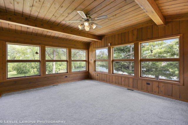 unfurnished sunroom featuring plenty of natural light, wooden ceiling, carpet, wooden walls, and beamed ceiling