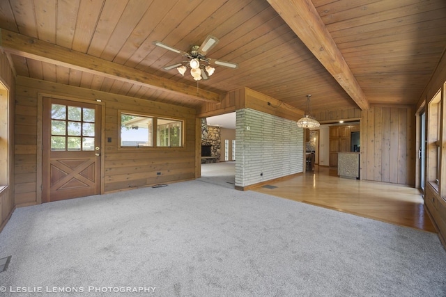 unfurnished living room featuring beam ceiling, wooden walls, wood ceiling, carpet flooring, and a ceiling fan