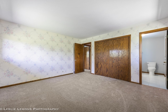 unfurnished bedroom featuring a closet, wallpapered walls, carpet floors, and ensuite bathroom