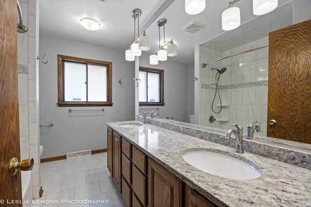 bathroom with toilet, a tile shower, baseboards, and double vanity