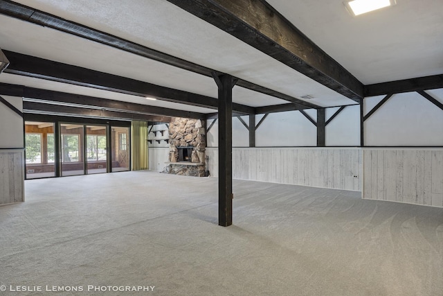 unfurnished living room with beamed ceiling, carpet flooring, wood walls, and a fireplace