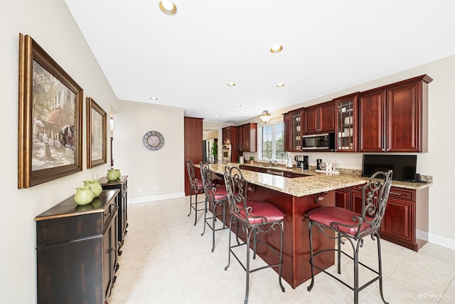 21359 Saddle Ln, Mokena, IL 60448 - kitchen featuring stainless steel microwave, reddish brown cabinets, a kitchen breakfast bar, baseboards, and glass insert cabinets