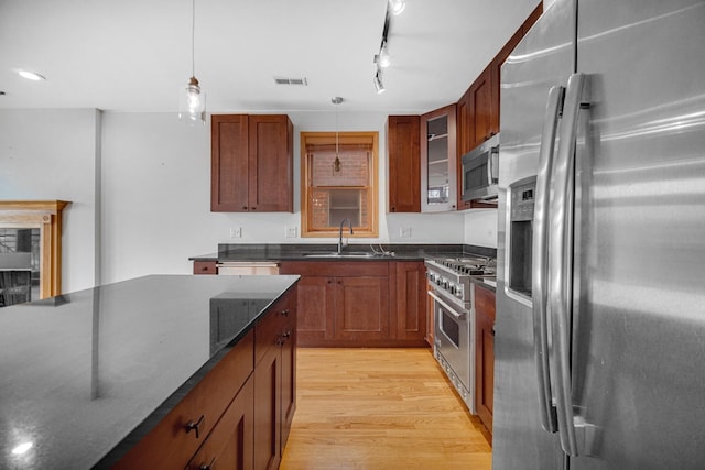 kitchen featuring stainless steel appliances, a sink, light wood-style floors, pendant lighting, and glass insert cabinets