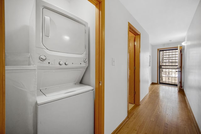 clothes washing area with estacked washer and dryer, light wood-style floors, and baseboards