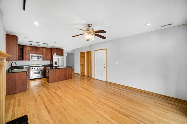 kitchen featuring stainless steel appliances, a sink, dark countertops, ceiling fan, and light wood-style flooring