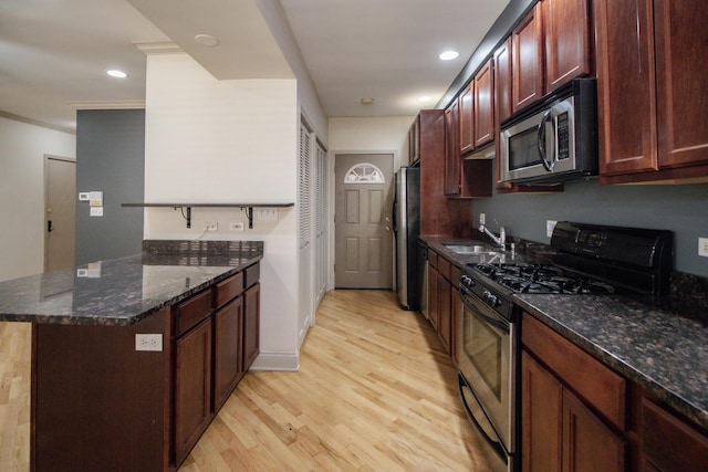 kitchen with appliances with stainless steel finishes, a sink, a peninsula, light wood-type flooring, and crown molding