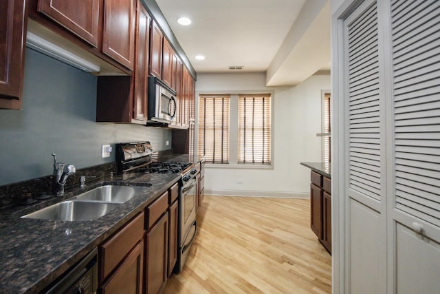 kitchen featuring stainless steel appliances, a sink, light wood-style floors, recessed lighting, and dark stone counters