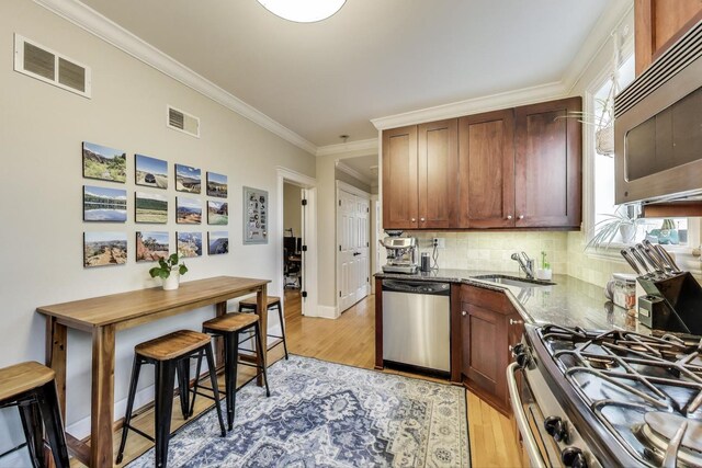 2336 W Roscoe St Unit 3R, Chicago, IL 60618 - kitchen featuring appliances with stainless steel finishes, light wood finished floors, a sink, backsplash, and ornamental molding