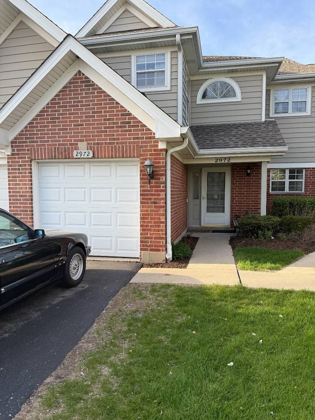 townhome / multi-family property featuring brick siding, asphalt driveway, a shingled roof, a garage, and a front lawn