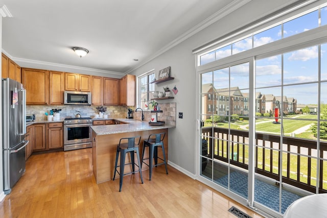 210 Station Park Cir, Grayslake, IL 60030 - kitchen featuring appliances with stainless steel finishes, ornamental molding, a peninsula, brown cabinetry, and light wood finished floors