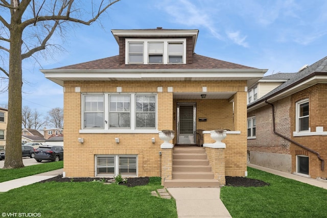 bungalow featuring brick siding, a front lawn, and roof with shingles