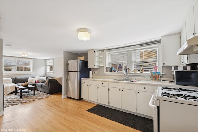 kitchen featuring stainless steel appliances, under cabinet range hood, a sink, light wood-style flooring, and white cabinets