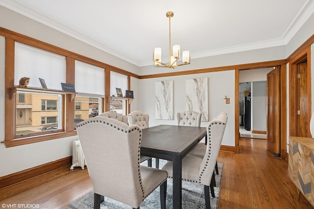 dining area featuring a chandelier, radiator, crown molding, baseboards, and wood finished floors