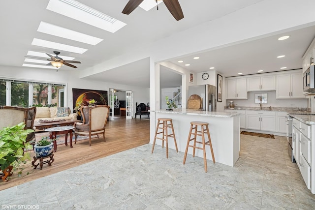 145 W Lake Shore Dr, Tower Lakes, IL 60010 - kitchen with stainless steel appliances, ceiling fan, a breakfast bar area, light stone countertops, and a skylight