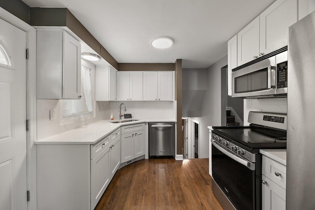 kitchen with appliances with stainless steel finishes, a sink, dark wood finished floors, light countertops, and white cabinets