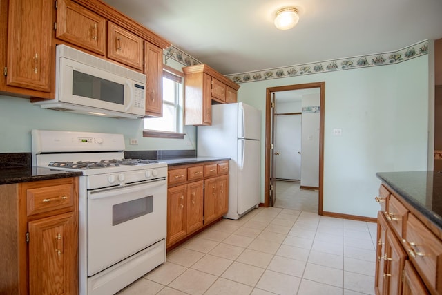 kitchen with white appliances, brown cabinetry, dark stone counters, and baseboards
